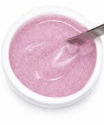 Top-down view of a pink glitter gel in a clear nail product pot with a metal spatula overlapping the surface to scoop product.