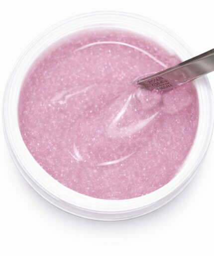 Top-down view of a pink glitter gel in a clear nail product pot with a metal spatula overlapping the surface to scoop product.