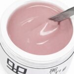 Open container of pink gel nail polish with a metal spatula stirring the glossy gel.