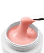 Pink cosmetic cream lifted from an open white jar by a black spatula, forming a soft ribbon of product.