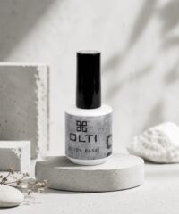 White nail polish bottle with a tall black cap labeled OLTI Beton Base on a circular concrete pedestal.