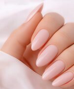 Close-up of almond-shaped nails with a glossy pale pink gel manicure on well-lit skin.