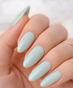 Close-up of a hand showing almond-shaped nails painted pale mint blue with a glossy finish.