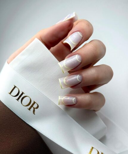 Close-up of a hand with pale pink glittery nails and white curved tips, holding a white Dior ribbon bowing around the fingers.