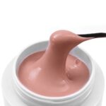 Close-up of a pale pink moisturizer being scooped from a white jar with a black spatula.