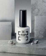 White bottle of Top Beton nail polish with a tall black cap, placed on a gray stone surface.